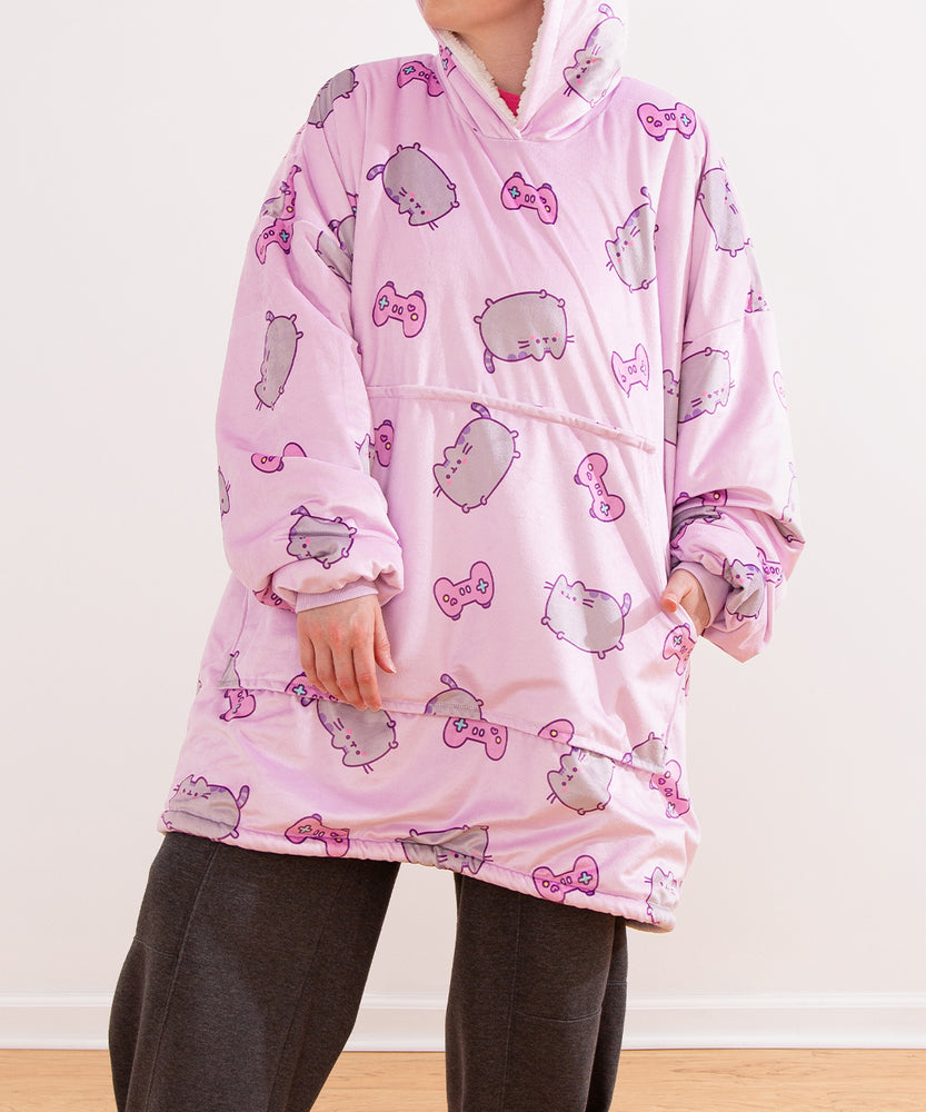 Front view of the model wearing the oversize blanket pullover sweater. The oversized sleeves are scrunched up to show the model’s hands. The large kangaroo style pocket sits towards the middle of the pullover. The hem of the sherpa-lined hoodie falls near the model’s knees. 