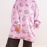 Front view of the model wearing the oversize blanket pullover sweater. The oversized sleeves are scrunched up to show the model’s hands. The large kangaroo style pocket sits towards the middle of the pullover. The hem of the sherpa-lined hoodie falls near the model’s knees. 