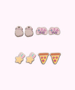 All earrings in Gaming Pusheen 4-Pack Stud Earrings Stud shown. From left to right and top to bottom, the stud earrings include Pusheen wearing headphones, a gaming controller, a shooting star, and pepperoni pizzas.  