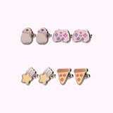 Earrings in the Stud Set turned to the side to show the shine of the outline of the stainless-steel edging. The set includes Pusheen wearing pink and mint green headphones, a pink and purple gaming controller, a yellow shooting star with purple, green, and pink streaks, and a yellow cheese pizza with a brown crust and pink pepperonis.  