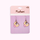 Gaming Pusheen Dangle Earrings on their cardboard backing card. The top half of the card has the Pusheen logo in brown on a light pink background and the bottom half of the card is purple. 