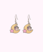 Front view of the Gaming Pusheen Dangle Earrings. Wearing pink and mint green headphones, Pusheen the Cat has light purple back stripes while sitting on a yellow crescent moon with a light pink star.  