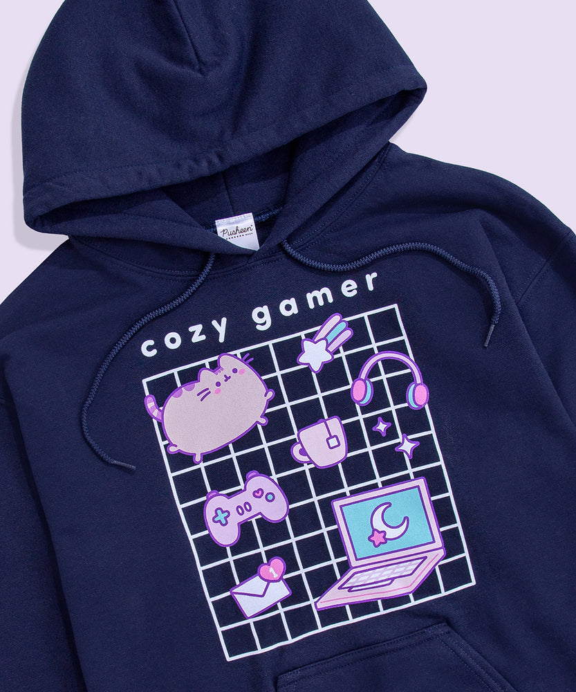 Full view of Gaming Pusheen Hoodie. The large, printed graphic in the center of the front of the sweatshirt features a white grid with Pusheen and her gaming essentials in front. Above the graphic is the phrase “cozy gamer.” 