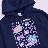 A close-up view of the Gaming Pusheen Hoodie screen print graphic. The grey and purple cat is shown blushing in the top left corner with her gaming necessities including headphones, a controller, and a laptop. 