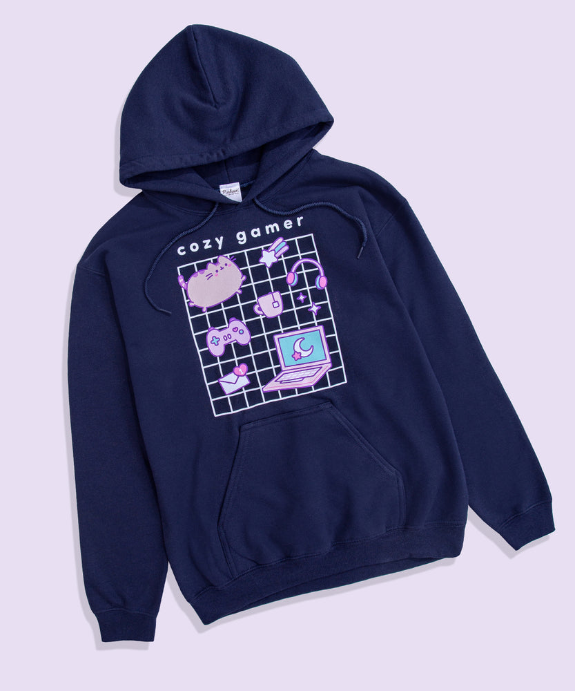 Full view of Gaming Pusheen Hoodie. The large, printed graphic in the center of the front of the sweatshirt features a white grid with Pusheen and her gaming essentials in front. Above the graphic is the phrase “cozy gamer.” 