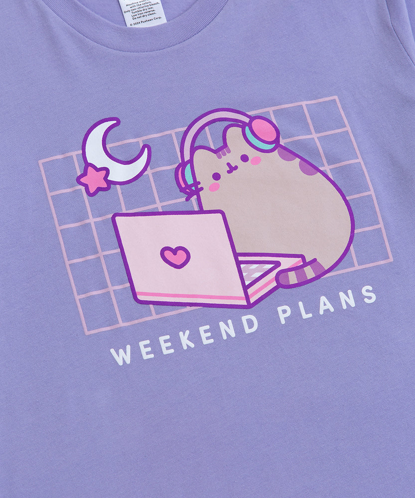 Front view of the Gaming Pusheen Tee. The light purple tee-shirt features a moon and star graphic in the top left corner of the front printed graphic. Under the graphic that spans the wearer’s chest is the phrase “Weekend Plans.” 