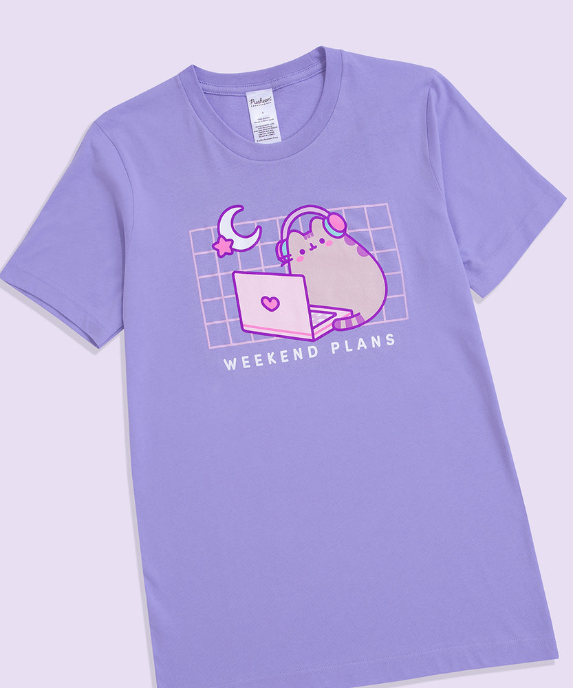 Front view of the Gaming Pusheen Tee. The light purple tee-shirt features a moon and star graphic in the top left corner of the front printed graphic. Under the graphic that spans the wearer’s chest is the phrase “Weekend Plans.” 