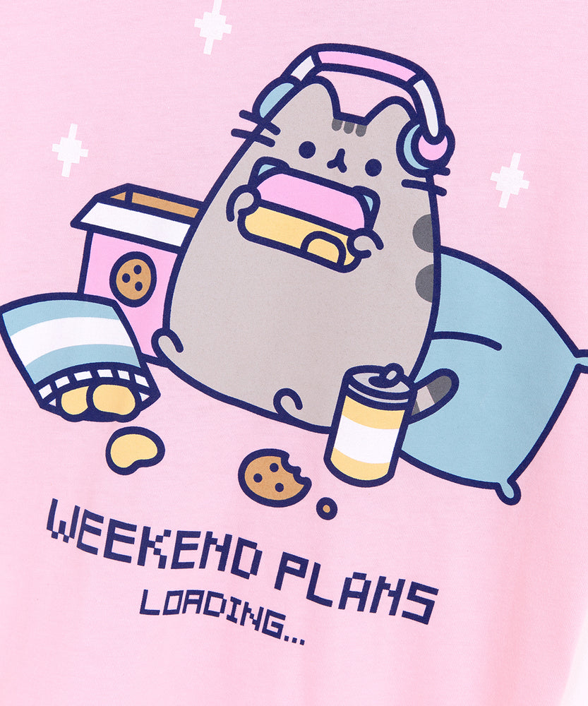 A close-up view of the Gaming Pusheen Weekend Plans Unisex Tee's screen print graphic. A focused Pusheen is shown holding a gaming controller and she’s surrounded by her favorite snacks including drinks, chips, and cookies. All print elements include the colors Grey, yellow, blue, pink, and navy blue. 