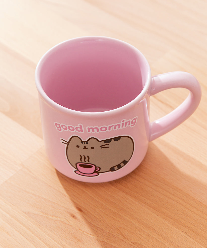 Back view of Pusheen pink mug. The light-pink cup features a grey and brown graphic of Pusheen relaxing with her own hot beverage in a pink mug. The graphic on the back matches the graphic on the front. 