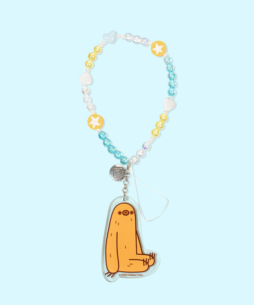    The Sloth Beaded Phone Charm lies on a blue background. The beaded string includes blue, yellow, and clear round beads, yellow round beads with white stars, and white and light blue heart-shaped beads. At the end of the string is an acrylic charm of Pusheen’s friend Sloth sitting.  