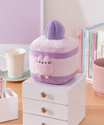 Cake Squisheen shown on a desktop to show scale of 7" tall plush toy. Pusheen the Cat rests inside the cream layer of the cake plush.