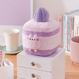 Cake Squisheen shown on a desktop to show scale of 7" tall plush toy. Pusheen the Cat rests inside the cream layer of the cake plush.