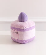 Side quarter view of the lavender cake Pusheen plush. The cake plush has a medium purple cake layer in the top and at the bottom of the square plush. 