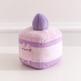 Side quarter view of the lavender cake Pusheen plush. The cake plush has a medium purple cake layer in the top and at the bottom of the square plush. 