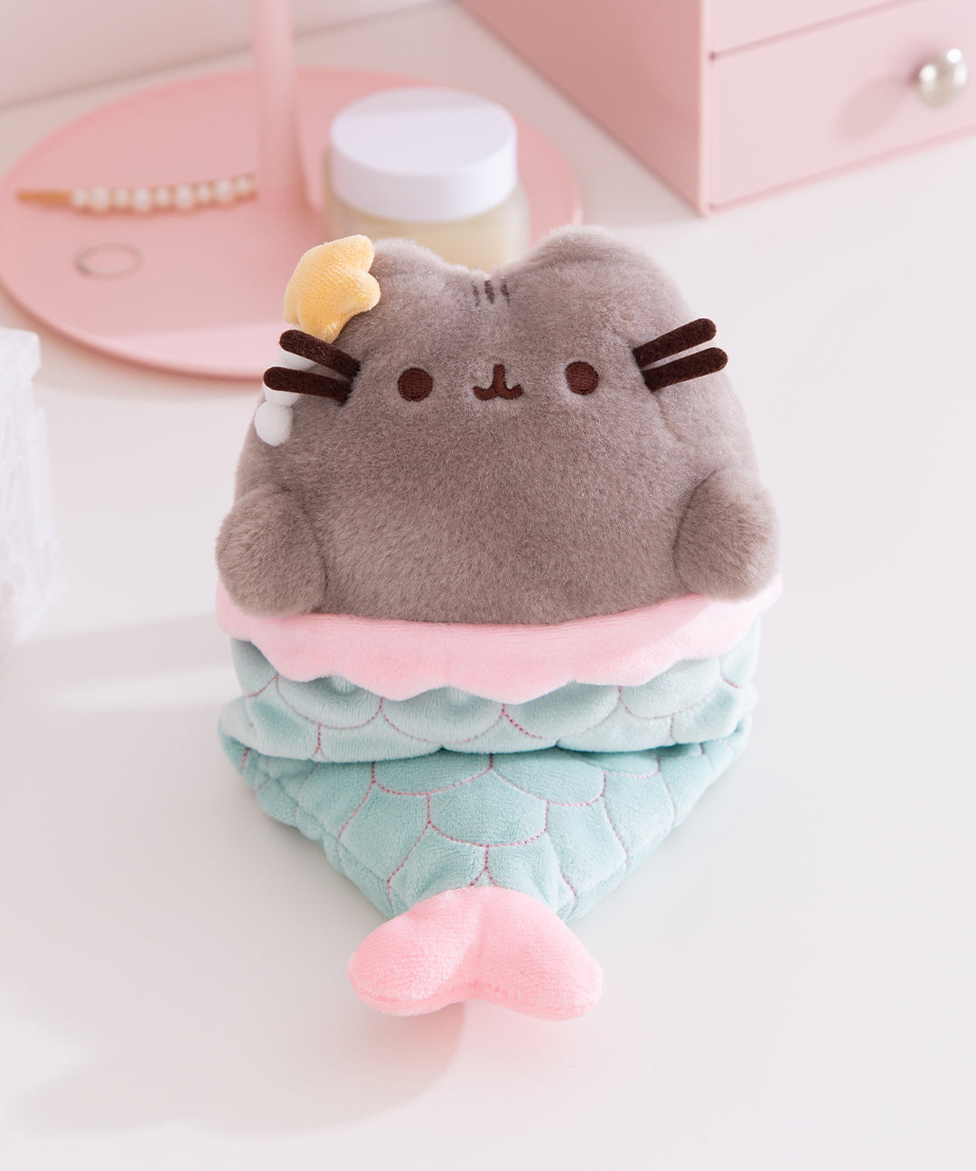 Front view of the Mermaid Pusheen Plush. The grey fluffy Pusheen wears a mint green and pink mermaid tail with embroidered scale details.