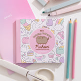 Mini coloring book with Pusheen and character illustrations on a white desktop with stationery items including pencils, scissors, and markers.