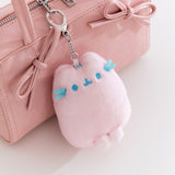 Pink plush keychain with blue accents attached to a pink handbag.
