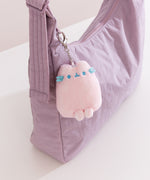 Pink plush keychain with blue accents attached to a purple bag.