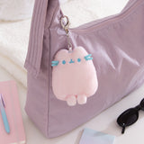 Plush keychain attached to a purple bag with a notebook and sunglasses on a light surface.