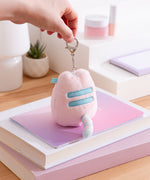 Model holds lobster claw clip keychain on the Pink Dreamsheen Bag Charm. The fluffy pink bag charm has light blue embroidery details. 