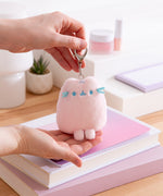 Model holds keychain and bottom of bag charm to show size and scale of the pink fluffy Pusheen keychain. 