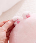 Close-up of a hand holding a pink plush toy with tiny pink paw prints on a light background.
