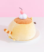 Back view of the pudding squisheen plush. Pusheen’s tail is stripped with light yellow and a warm light brown. Little yellow paws extend off the back of the pudding plush and hang over the white plate that the flan plush is sitting atop. 