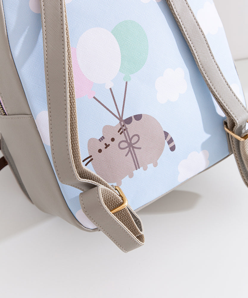 Close-up of the back graphic on the backpack that shows Pusheen the Cat floating through puffy clouds attached to pink, white, and mint green balloons.
