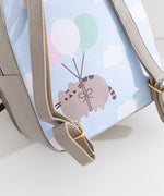Close-up of the back graphic on the backpack that shows Pusheen the Cat floating through puffy clouds attached to pink, white, and mint green balloons.