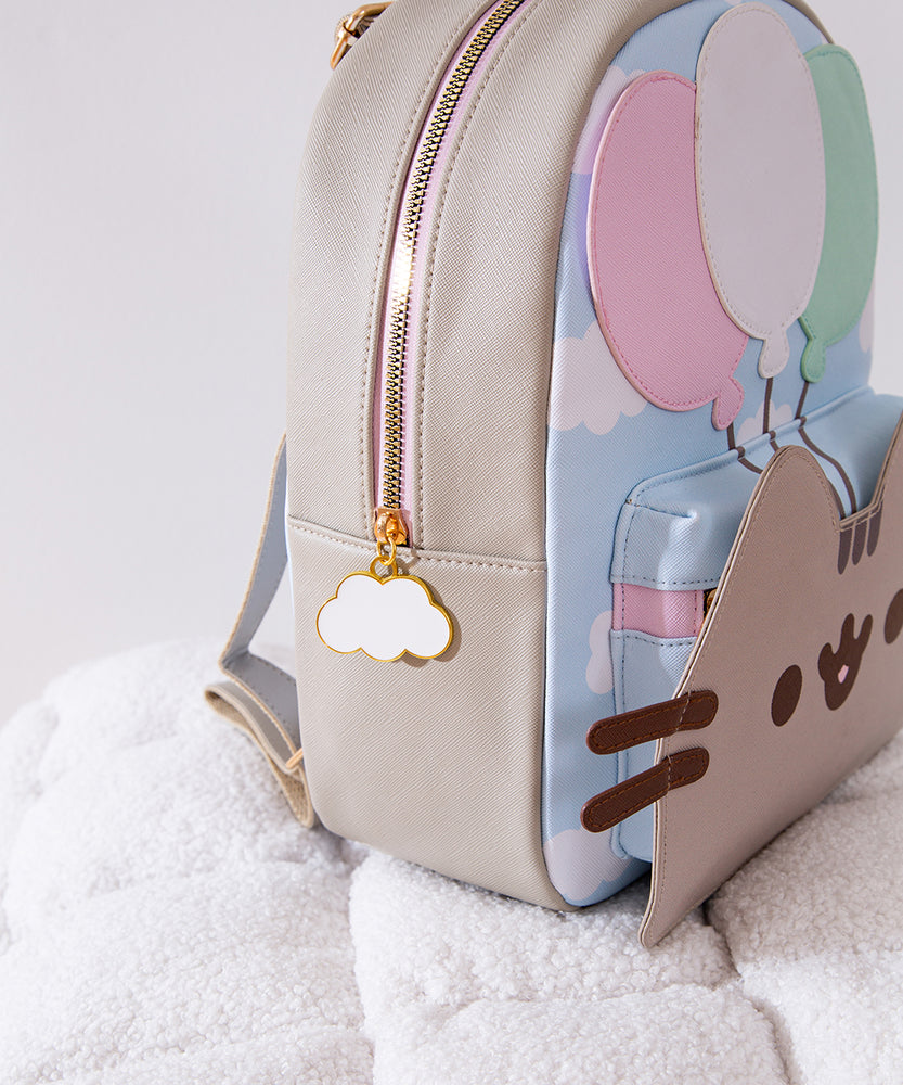 Close-up side view of the backpack. The gold and pink zipper has a white cloud zipper charm pull outlined in gold. 