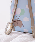 Close-up view of the adjustable straps and back graphic on the anniversary backpack. The back graphic shows Pusheen the Cat floating through puffy clouds attached to pink, white, and mint green balloons. 