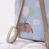 Close-up view of the adjustable straps and back graphic on the anniversary backpack. The back graphic shows Pusheen the Cat floating through puffy clouds attached to pink, white, and mint green balloons. 
