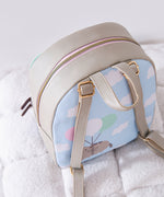 Top aerial view of the backpack and cloud motif back graphic. The grey backpack has a pink and gold zipper. 