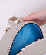 Model holds open top zipper of the cat backpack to show blue interior.