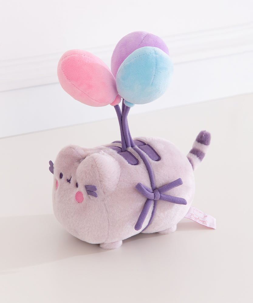 Quarter side view of the Pusheen 15th Anniversary Balloons Plush toy. Pusheen the cat is tied to three multi-colored balloons. Her normally brown details are dark purple.