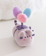Aerial view of the plush toy showing Pusheen the Cat blushing while attached to blue, purple, and pink plush balloons. 