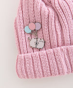 Pink knit beanie with a cat deluxe pin attached. The cat is attached to three colorful balloons with a bow.