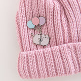 Pink knit beanie with a cat deluxe pin attached. The cat is attached to three colorful balloons with a bow.