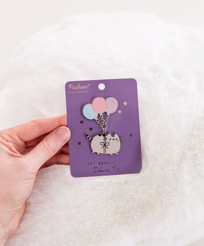 Pusheen pin with balloons on a purple card against a white fur background.