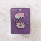 Pusheen pin with balloons on a purple card against a white fur background.
