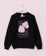 The Pusheen 15th Anniversary Tee hangs on a light pink hanger. The black sweatshirt features a large graphic of Pusheen with a trio of balloons and surrounded by fireworks.