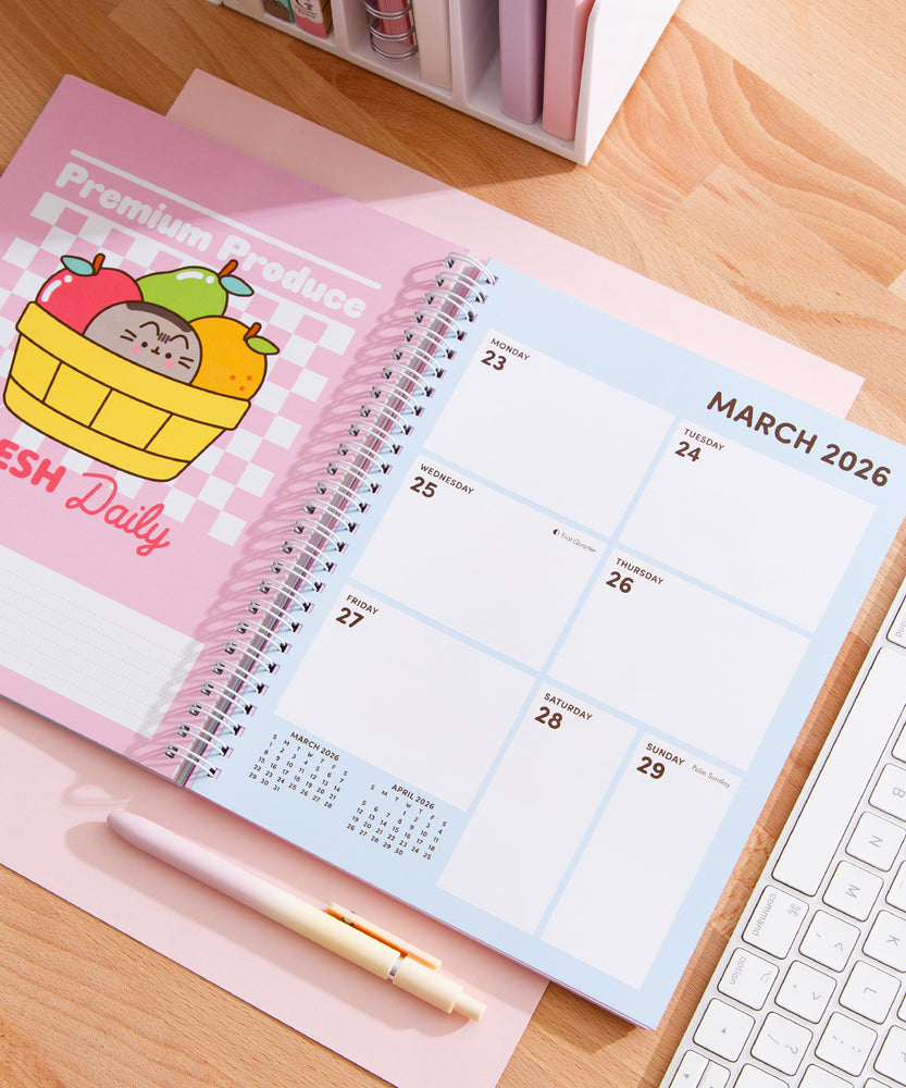 Open planner to March 2026. The fruit themed calendar page is paired with a 7-day calendar view. The planner lies on a wooden desk next to a pen and keyboard.