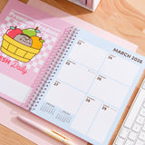 Open planner to March 2026. The fruit themed calendar page is paired with a 7-day calendar view. The planner lies on a wooden desk next to a pen and keyboard.