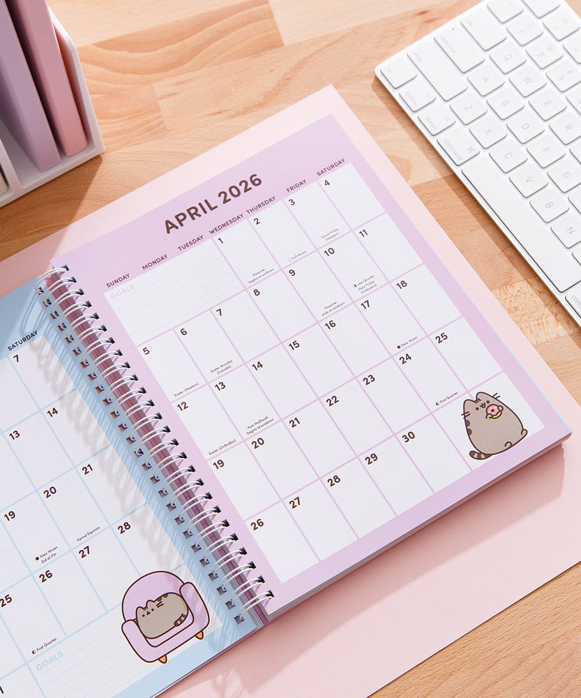 Full month calendar view for April 2026 in the Pusheen 2025-2026 16-Month Planner. In the right bottom corner of the page is a graphic of Pusheen the Cat holding a pink glazed donut. 