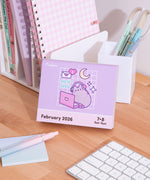 Pusheen 2026 Daily Desk Calendar page for the weekend days of February 7-8, 2026. The graphic on this page shows Pusheen wearing headphones and sitting in front of a pink laptop with stars, moon, and envelope icons surrounding the pastel cat.