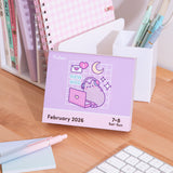 Pusheen 2026 Daily Desk Calendar page for the weekend days of February 7-8, 2026. The graphic on this page shows Pusheen wearing headphones and sitting in front of a pink laptop with stars, moon, and envelope icons surrounding the pastel cat.