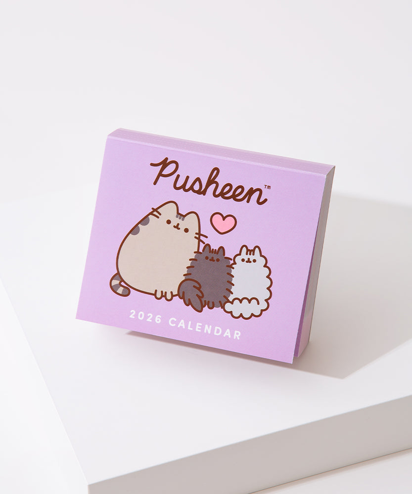 Front view of the front cover of the Pusheen 2026 day-to-day calendar. The purple cover shows a graphic of three gray cats. 