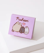 Front view of the front cover of the Pusheen 2026 day-to-day calendar. The purple cover shows a graphic of three gray cats. 