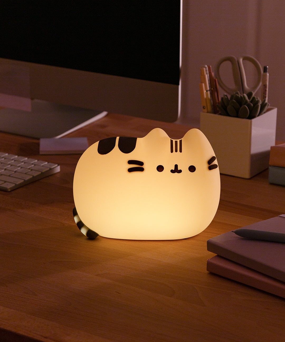 Pusheen 3D Lamp is illuminated on a desktop. The silicone lamp provides a soft glow light.