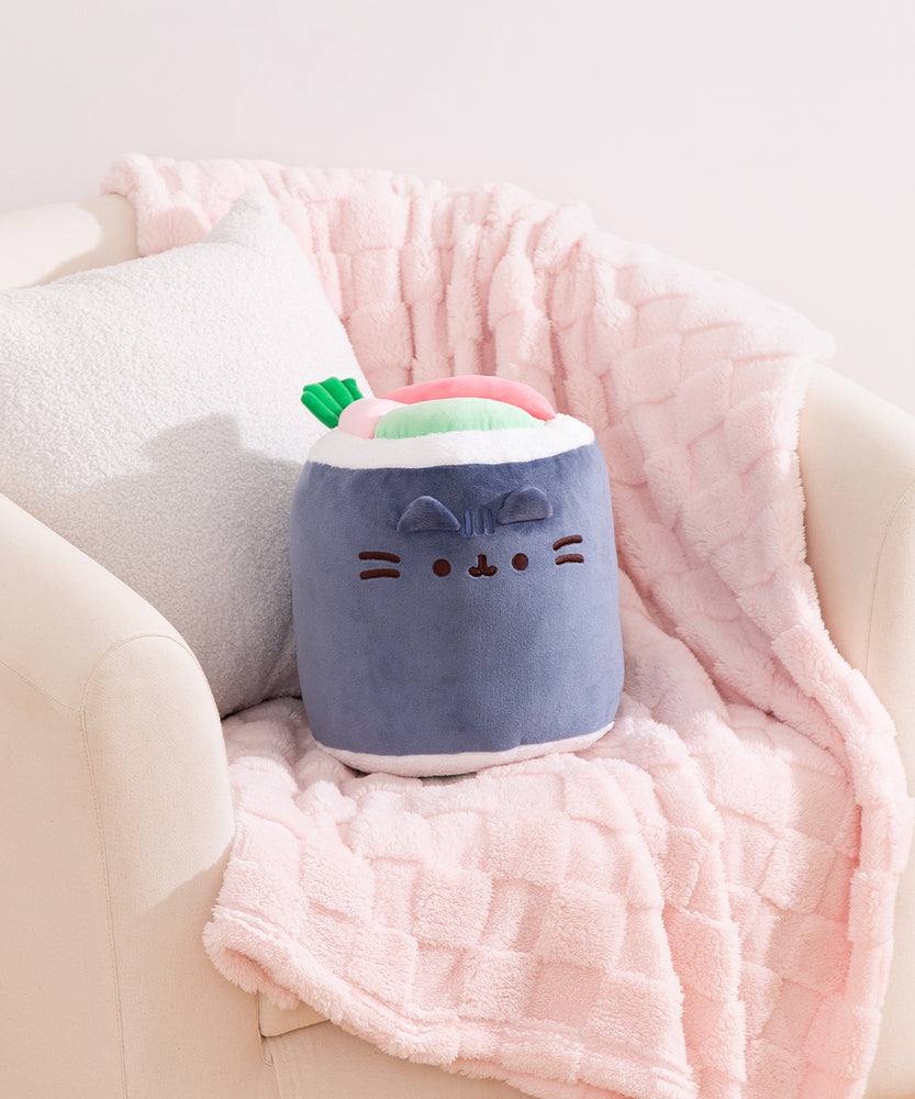 Black, white, green, and pink sushi roll plush sits on a chair to show size of plush.